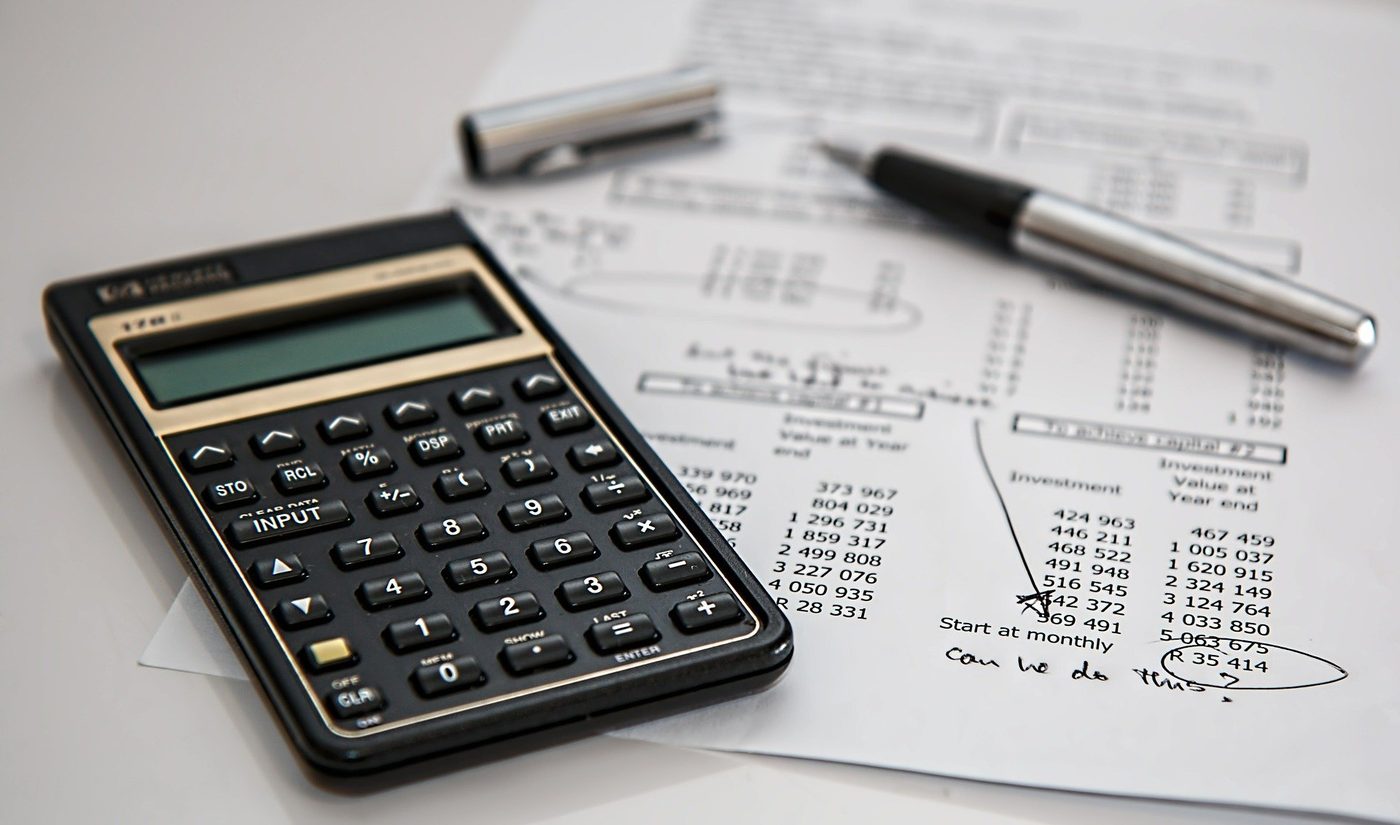 Photo of a calculator and a list of investment calculations with an uncapped pen at top.